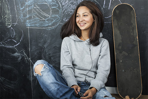 Photo of teenage girl in classroom at blackboard seating on table smiling